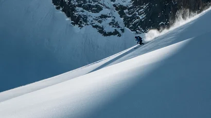 Skifahrer fährt einen steilen, verschneiten Berghang hinab