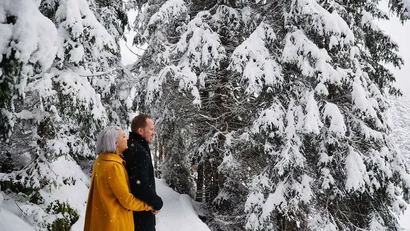 Paar steht im Schnee und schaut auf verschneite Tannenbäume