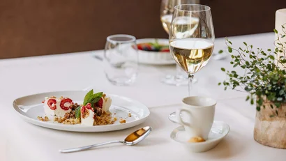 Dessertteller mit Beeren, Minzblatt, Glas Sekt und Kaffeetasse auf gedecktem Tisch