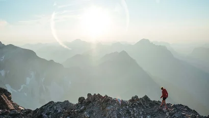 Wanderer auf felsigem Gipfel bei Sonnenaufgang in den Bergen