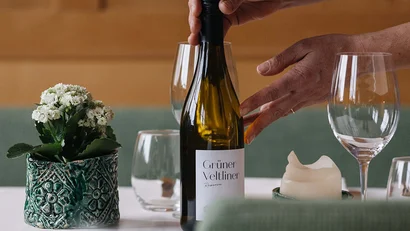 Person stellt eine Flasche Grüner Veltliner Wein auf einem gedeckten Tisch ab