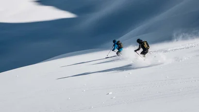 Zwei Skifahrer fahren auf verschneitem Berghang