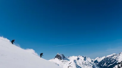 Zwei Skifahrer fahren einen schneebedeckten Berghang bei klarem Himmel hinunter