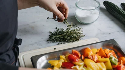 Person würzt farbenfrohes Gemüse mit frischen Kräutern auf Küchenarbeitsplatte