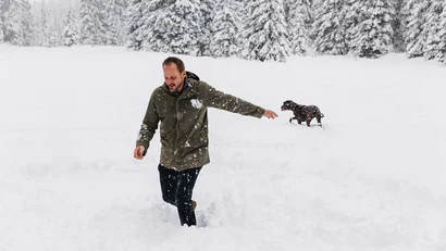 Mann spielt mit Hund im tiefen Schnee vor verschneiten Tannen