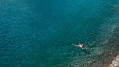 Person schwimmt im klaren, blau-grünen Wasser nahe felsigem Ufer