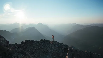 Person steht mit Hund auf Berggipfel bei Sonnenaufgang über Bergketten