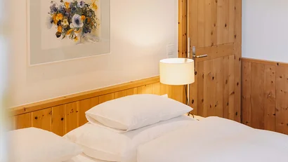 Helles Schlafzimmer mit Holztür, Bett und Blumenbild an der Wand