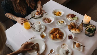 Frühstückstisch mit Croissants, Brot, Müslischalen, gekochten Eiern und Saft