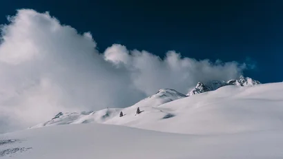 Verschneite Berglandschaft mit Bäumen und Wolken am blauen Himmel