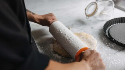 Person rollt Teig mit Nudelholz auf bemehlter Oberfläche aus