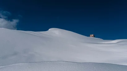 Schneebedeckter Hügel mit kleinem Holzhaus unter klarem blauem Himmel