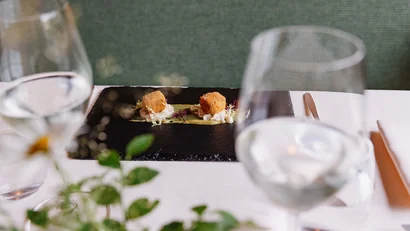 Zwei kleine frittierte Häppchen auf schwarzem Teller, Tisch elegant gedeckt