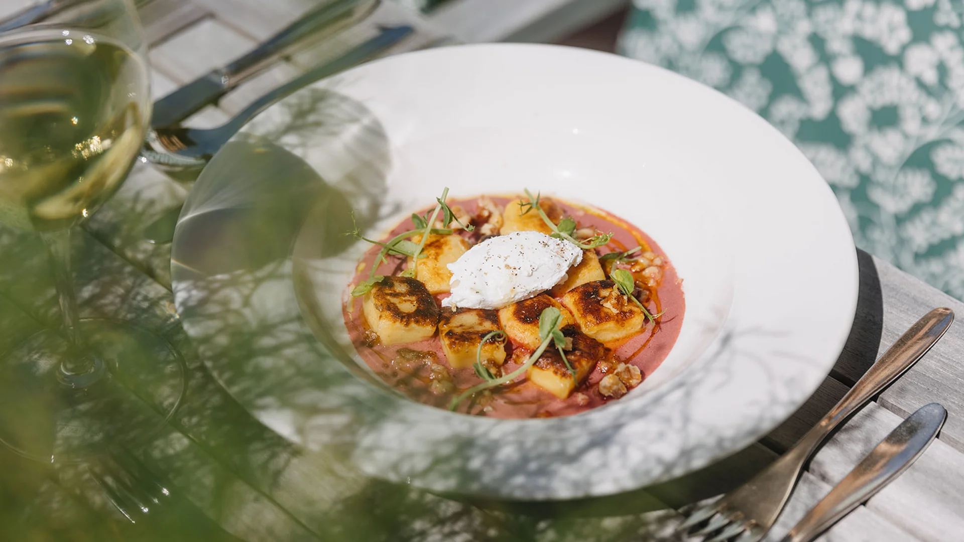 Gegrillte Gnocchi mit Sauce und Kräutern in weißer Schüssel neben Besteck und Glas