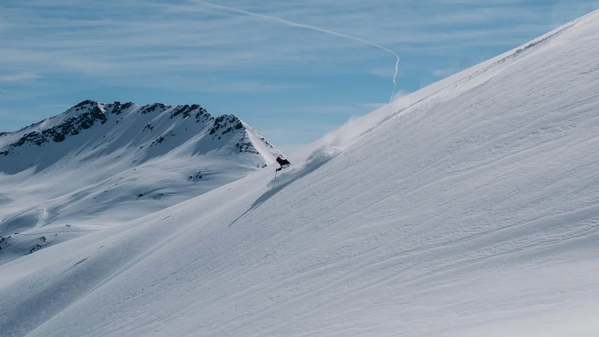 Skifahrer fährt einen steilen schneebedeckten Hang in den Bergen hinunter
