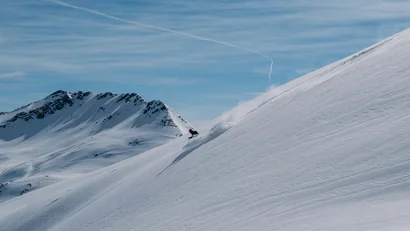 Skifahrer fährt einen steilen schneebedeckten Hang in den Bergen hinunter