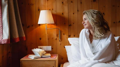 Frau in Bademantel sitzt auf Bett in gemütlichem Holzzimmer