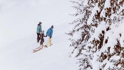 Drei Personen ziehen einen Schlitten durch schneebedeckten Wald