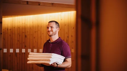 Mann hält gefaltete weiße Handtücher in einem warm beleuchteten Raum