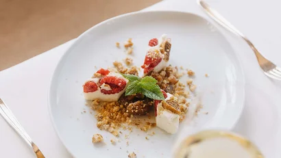 Dessert mit Himbeeren, Keksstücken und Minzblatt auf weißem Teller