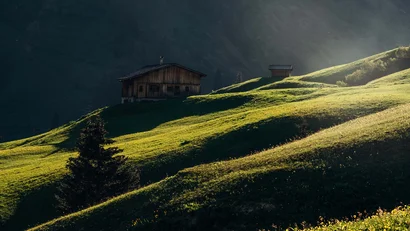 Hütte auf grünen Hügeln mit Berglandschaft im Hintergrund