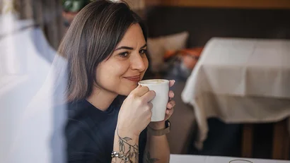 Frau mit Tattoos trinkt Kaffee beim Frühstück in einem Restaurant