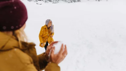 Zwei Frauen spielen im Schnee, eine hält eine Schneeball