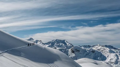 Skifahrergruppe auf verschneitem Berg mit Alpen im Hintergrund