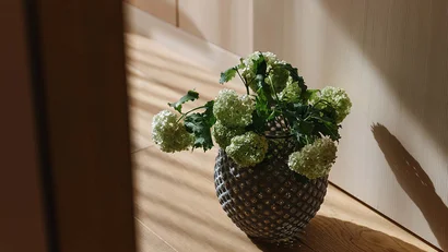 Vase mit weißen Blumen auf Holzboden vor hellem Holzpaneel