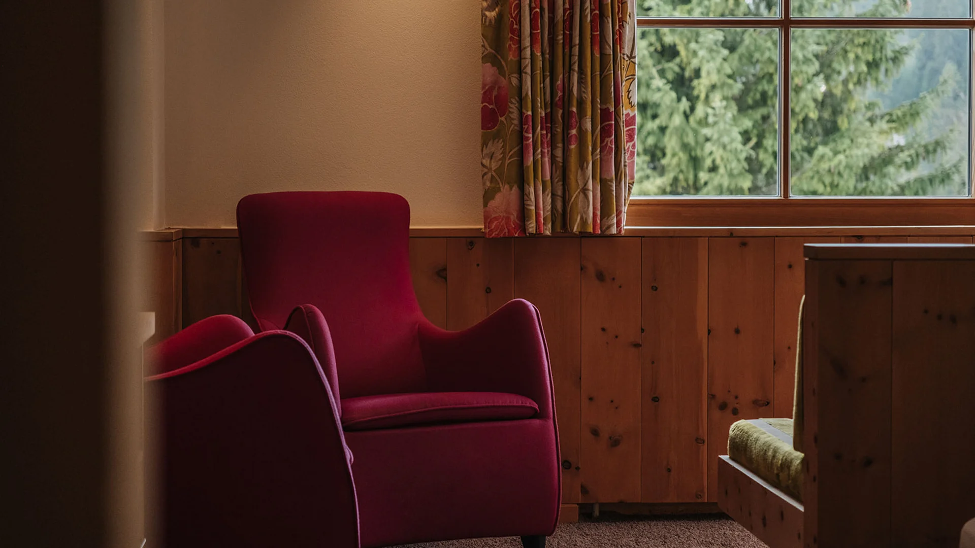 Gemütlicher roter Sessel neben Fenster und bunten Vorhängen im Zimmer