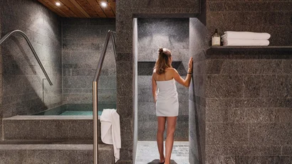 Frau in weißem Handtuch betritt Spa-Duschbereich mit Steinwänden
