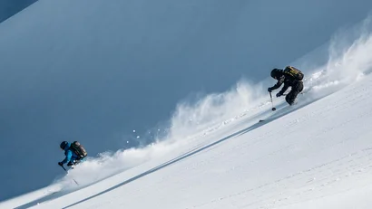Zwei Skifahrer fahren einen verschneiten Hang bergab