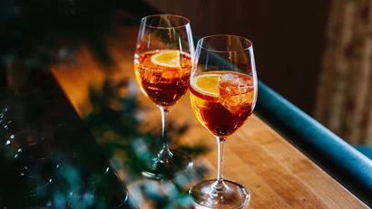 Zwei Gläser Aperol Spritz mit Orangenscheiben auf Holztheke