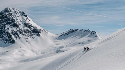 Zwei Skifahrer auf schneebedecktem Berghang bei klarem Himmel