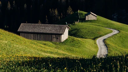 Holzhütten auf grünen Hügeln mit gewundener Straße im Sonnenlicht