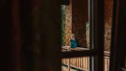 Frau lehnt auf Holzgeländer eines Hauses mit Holzverkleidung