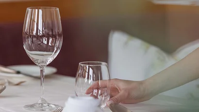 Hand nimmt Wasserglas an gedecktem Esstisch mit Weinglas und Besteck