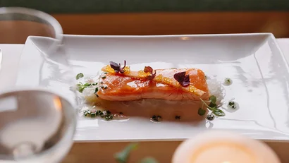 Gekochtes Lachsfilet auf weißem Teller mit Garnitur und Kerze im Vordergrund