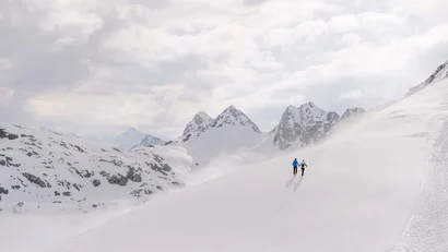 Zwei Personen wandern im verschneiten Berggebiet mit bewölktem Himmel