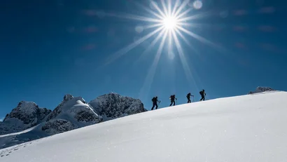 Vier Wanderer steigen bei strahlendem Sonnenschein in schneebedeckten Bergen auf