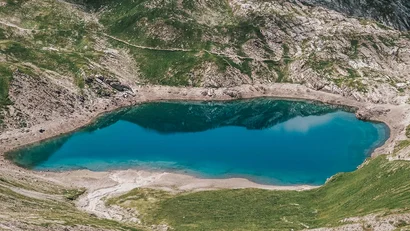 Blauer Bergsee umgeben von Felsen und grünem Gras